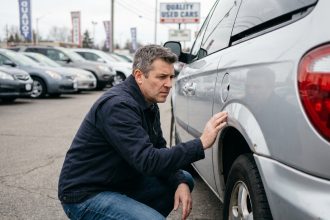 Homme inspectant la carrosserie d'un monospace 7 places d'occasion dans un parking de concessionnaire