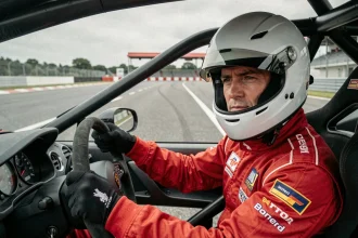 Instructeur de pilotage en combinaison rouge au volant d'une voiture de sport sur circuit professionnel