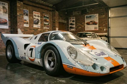 Porsche 917 Gulf Oil dans un garage musée patrimonial, reflet sur tarmac mouillé, ambiance historique Le Mans